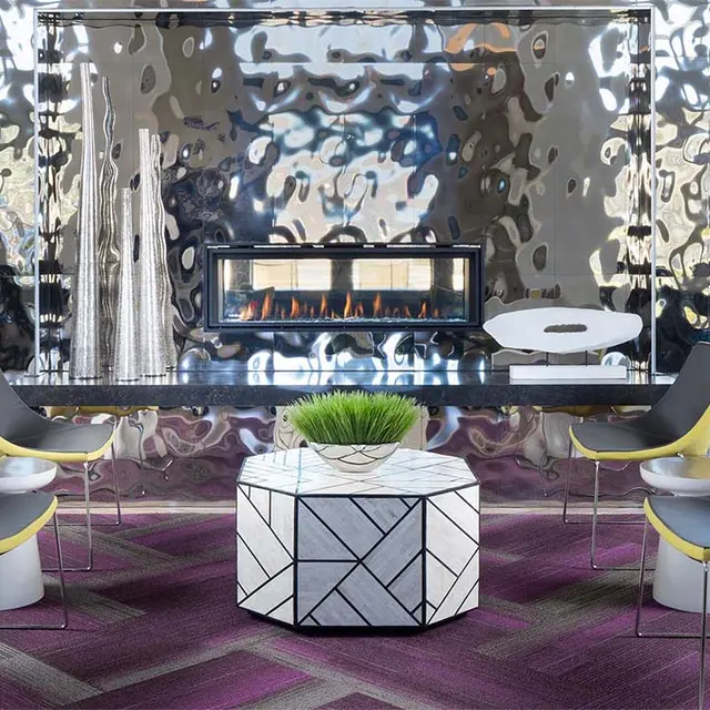 A contemporary living space featuring a shiny metallic accent wall, a modern fireplace, and stylish seating arrangements around a geometric coffee table on a patterned rug.