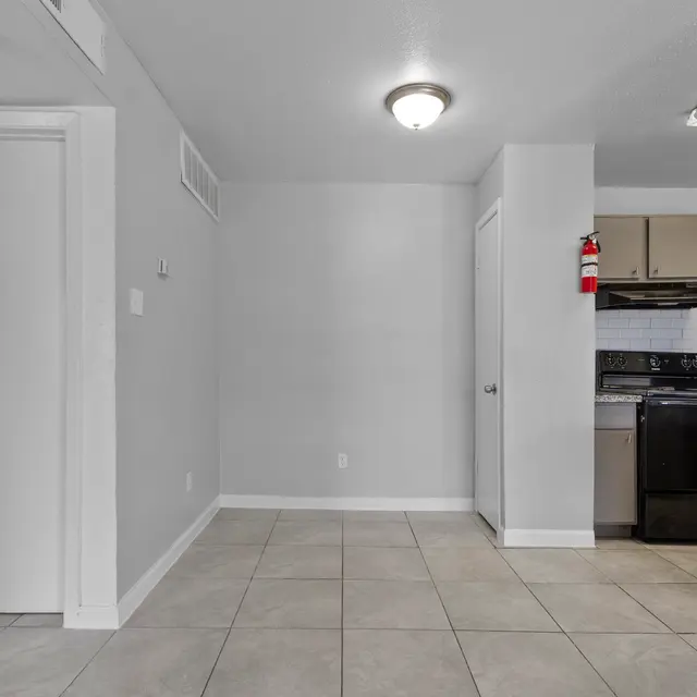 A modern kitchen interior featuring gray walls, tiled floor, and an open layout. The kitchen includes black appliances, a countertop, and storage cabinets.