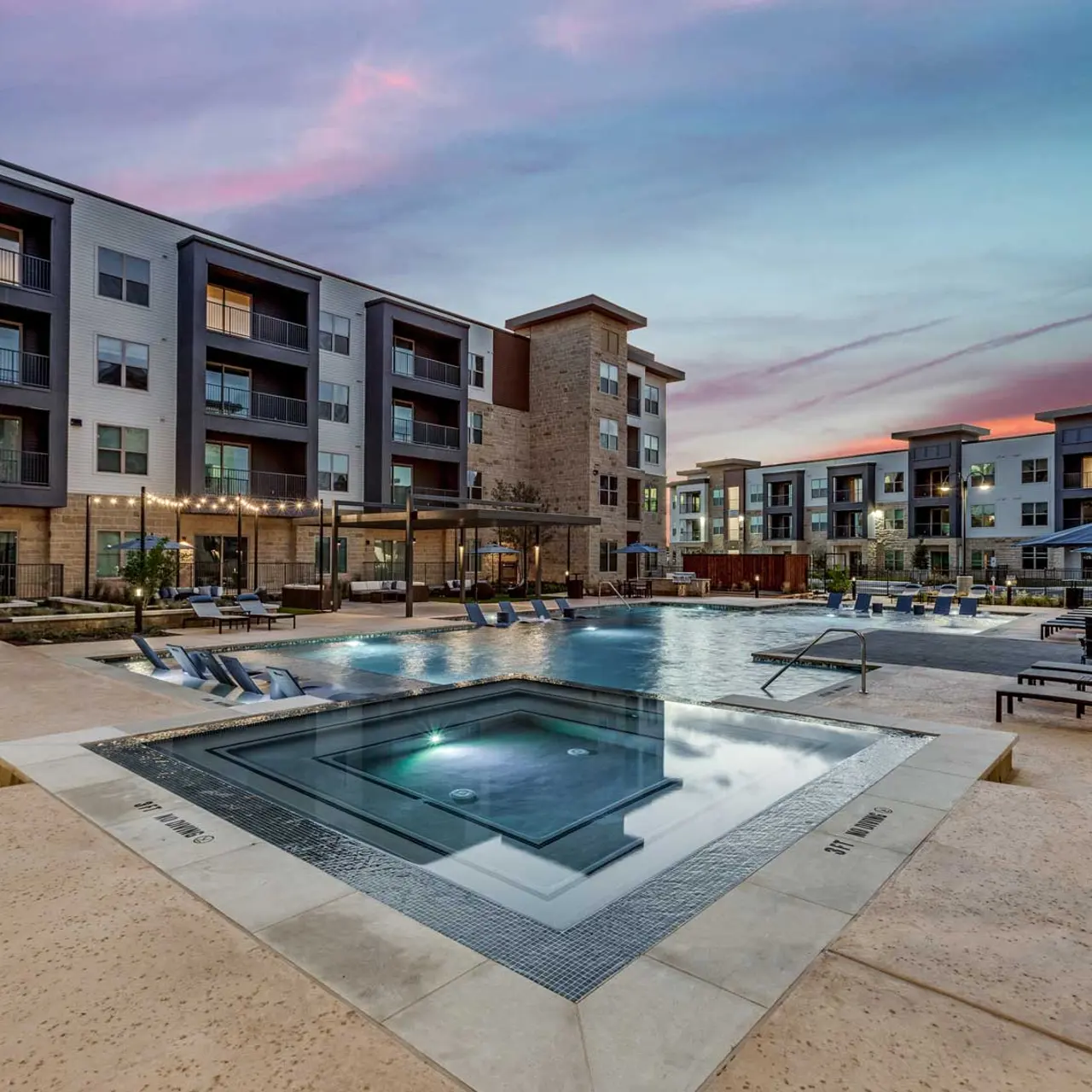 Luxury Apartment Complex Pool Area at Dusk A luxurious apartment complex featuring a large swimming pool surrounded by lounge chairs and beautiful landscaping during sunset.