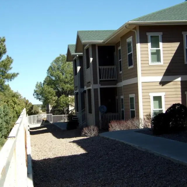 A view of an apartment building with a pathway leading up to it, surrounded by trees and shrubbery.