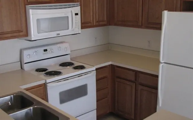 Modern Kitchen Design A modern kitchen featuring wooden cabinets, a white stove with four burners, a microwave above it, and a white refrigerator. The countertop is beige and there are two sinks to the left of the stove.