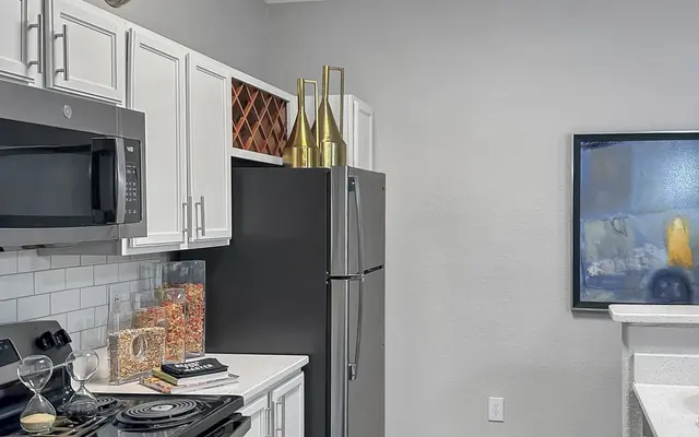 A modern kitchen featuring white cabinets, a black stove, a stainless steel refrigerator, and a framed artwork on the wall.