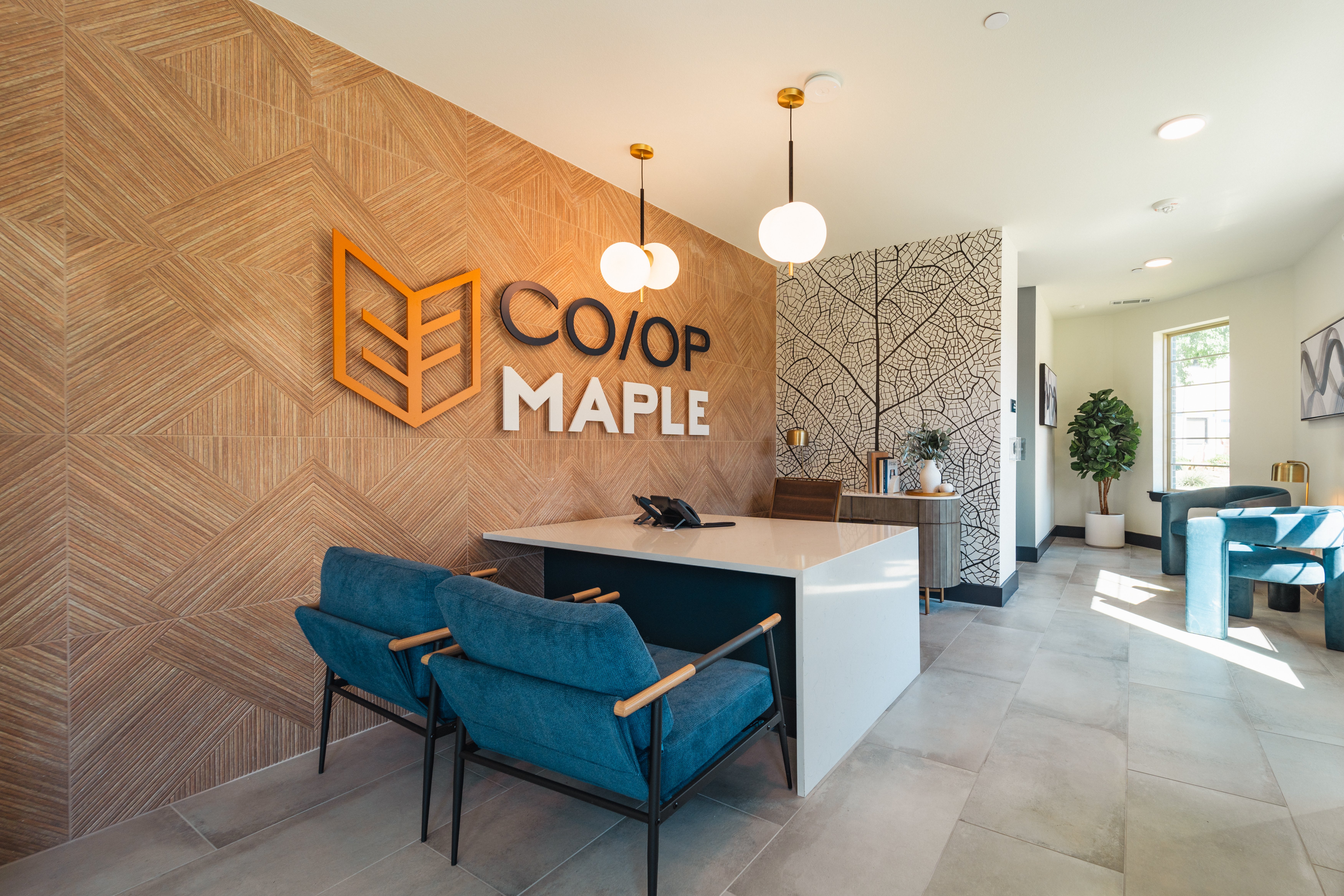 CO/OP Maple Reception Area Modern reception area featuring a wooden accent wall with the text 'CO/OP MAPLE', stylish seating, and decorative elements including a plant and artwork.