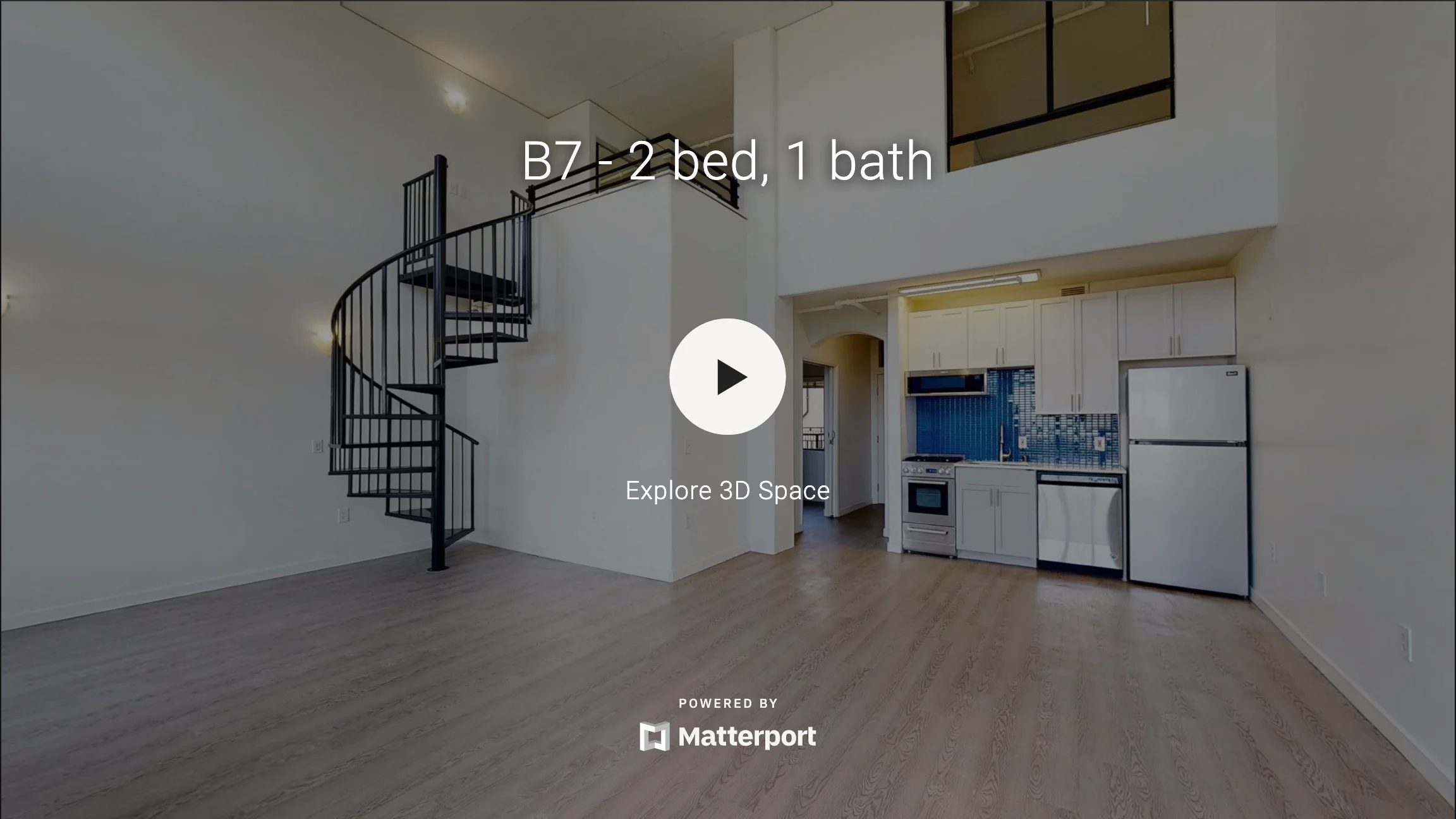 Interior view of a modern apartment featuring a spiral staircase, an open living area, and a kitchenette.