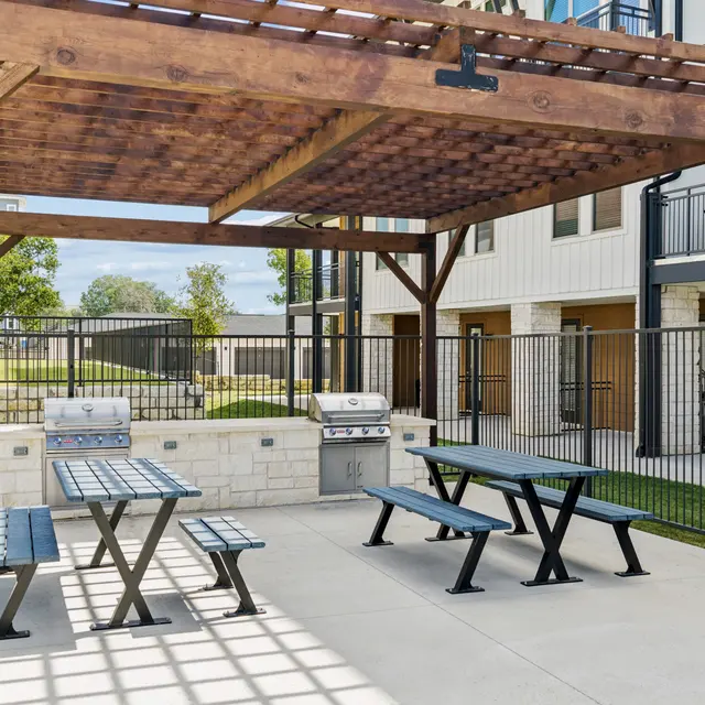 Community Barbecue Area Outdoor barbecue area with picnic tables and grills under a wooden pergola.