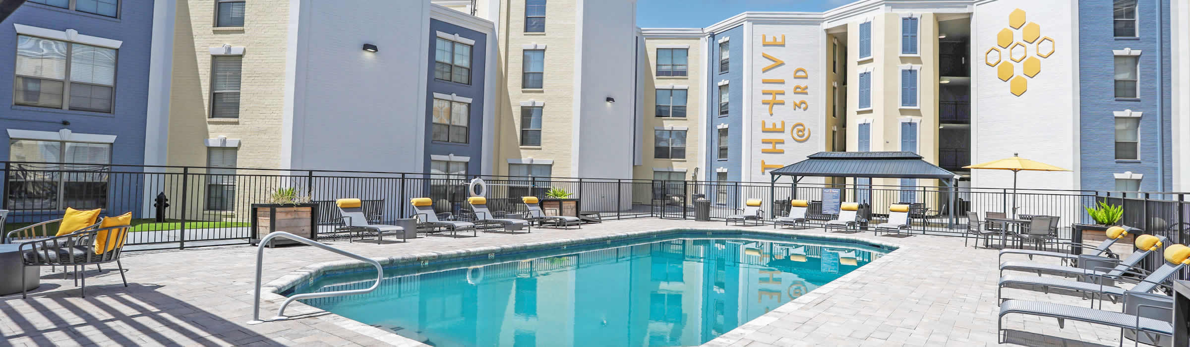 Swimming pool area at The Hive apartments with lounge chairs and surrounding buildings