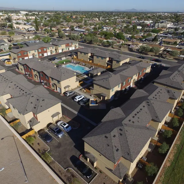 Modern Apartment Complex Aerial View Aerial view of a modern apartment complex featuring several buildings arranged around a central pool area, surrounded by landscaped grounds and parking spaces.