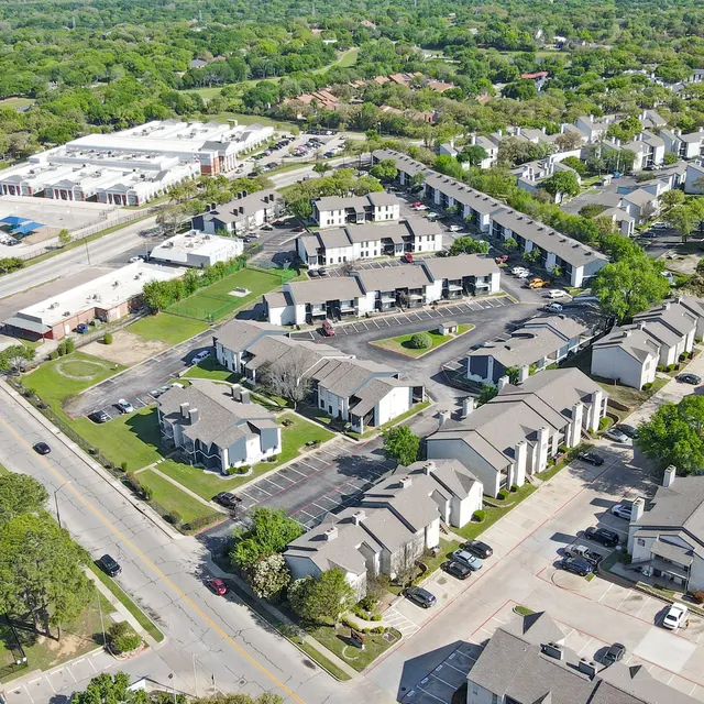 Aerial view of a suburban neighborhood showing residential buildings, parking areas, and greenery.