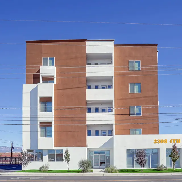 A modern apartment building with a brown and white facade, featuring five stories and large windows. Green landscaping in front and power lines in the background.