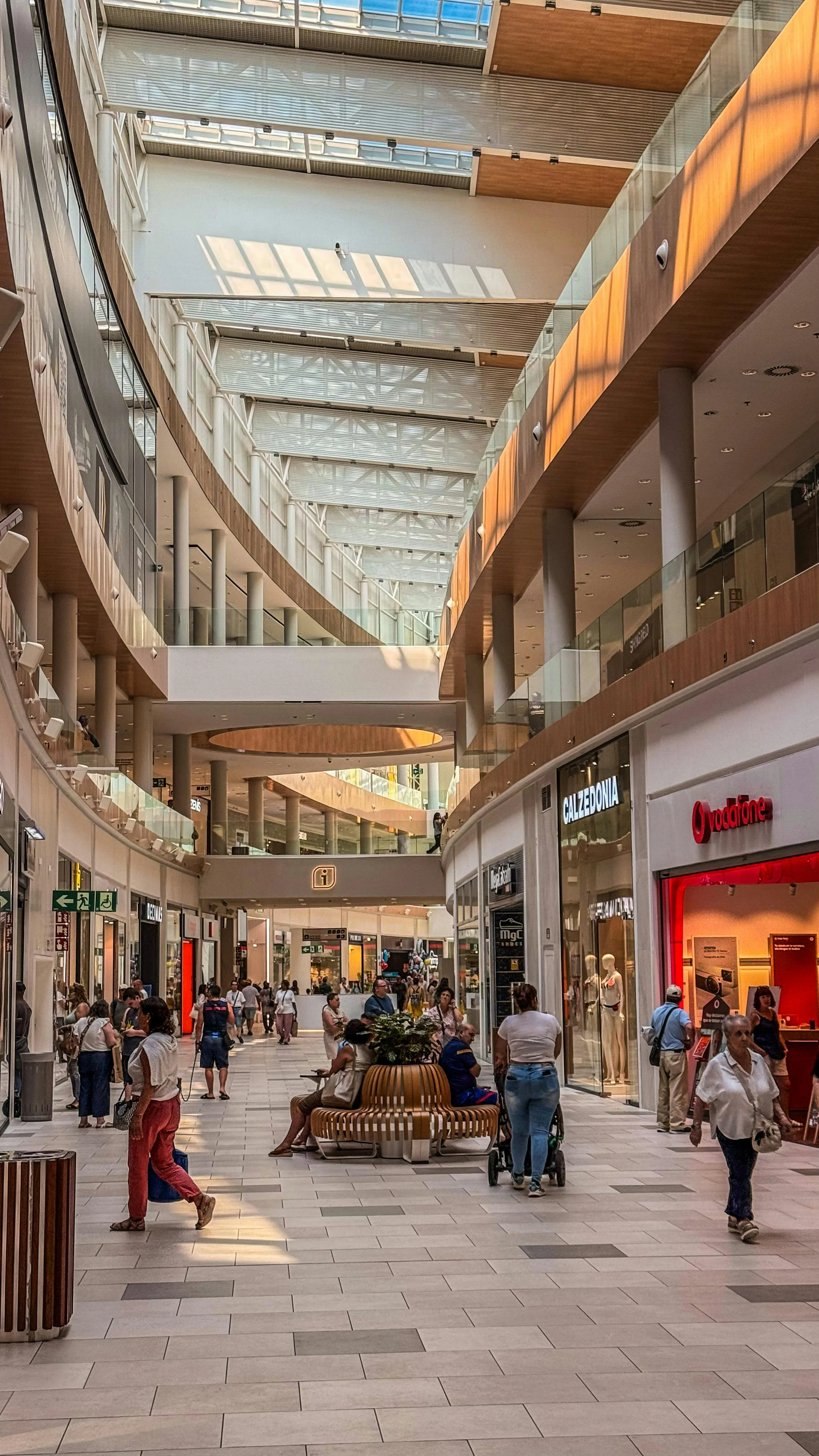 Interior of a Modern Shopping Mall Interior of a shopping mall with modern architecture, featuring a spacious walkways and shops on either side. Natural light coming through the roof.