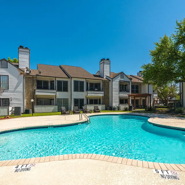 A clear blue swimming pool surrounded by apartment buildings and green landscaping.