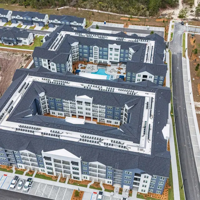 New Apartment Complex Overview Aerial view of a large, modern apartment complex with multiple buildings and a central courtyard featuring a pool. Surrounding areas include under-construction sections and landscaping.