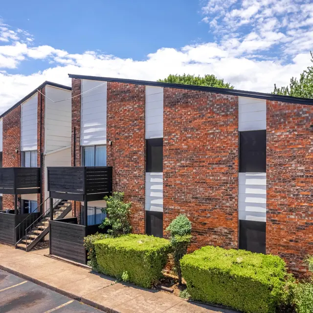 Exterior view of a brick apartment building with landscaping and a blue sky.