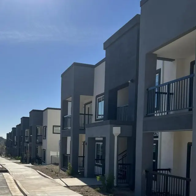 Row of modern apartment units with balconies and walkways under a clear blue sky.