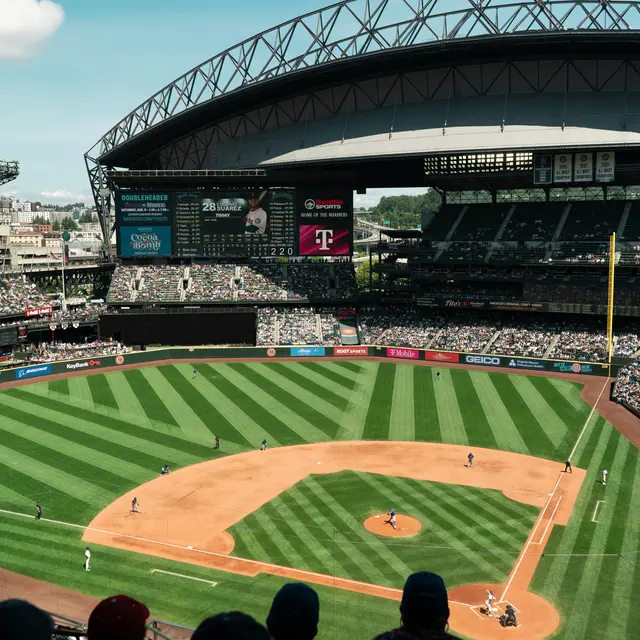 Daikin Park A wide view of a baseball stadium during a game, featuring a well-maintained field with vibrant green grass, a large roof overhead, and a crowd of spectators in the stands.
