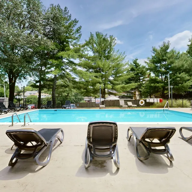 The Hideaway -  A clear blue swimming pool surrounded by lounge chairs, with trees and a building nearby under a blue sky.