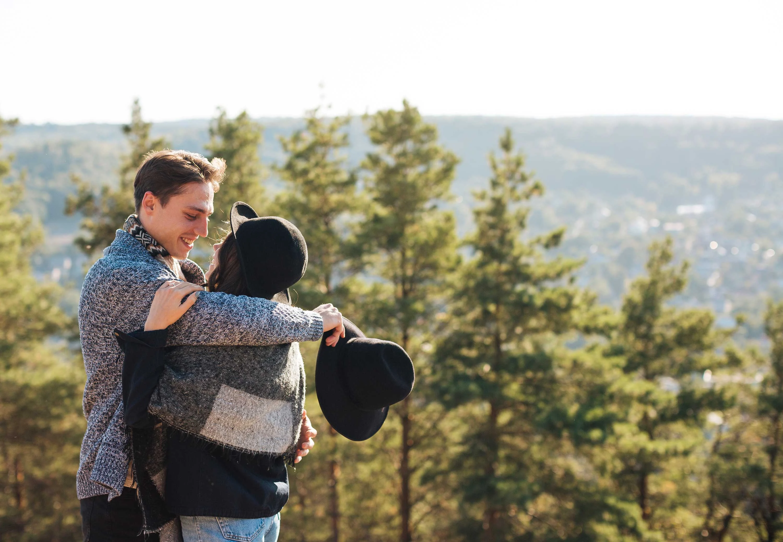 Embracing Nature A couple embracing outdoors with a scenic view of trees and hills in the background.