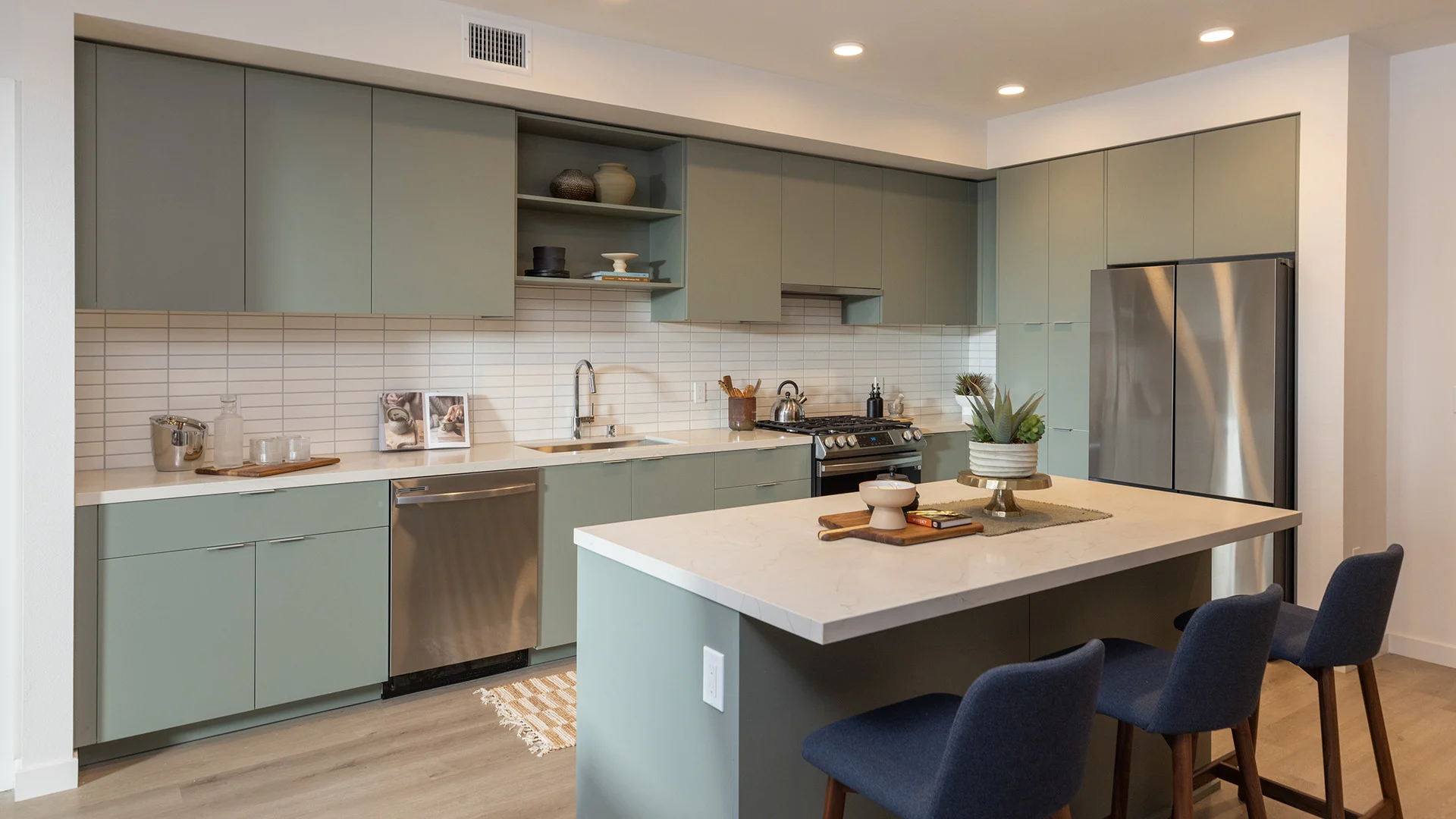 A modern kitchen featuring light green cabinets, stainless steel appliances, and a spacious island with seating.