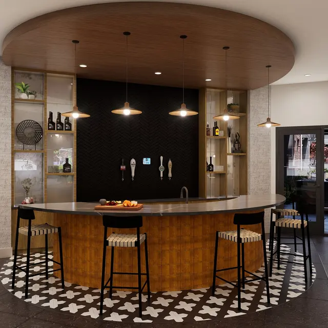 A contemporary bar area with an oval ceiling, wooden cabinetry, and high chairs. The bar features a marble countertop and is decorated with wine bottles and decorative items. A black and white patterned floor complements the stylish design.