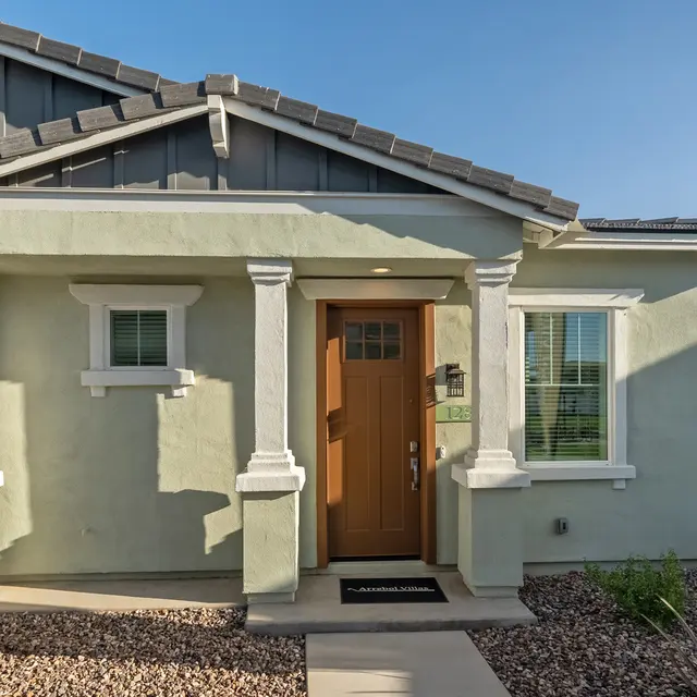 Exterior view of a modern single-story home with light green walls and a brown front door.