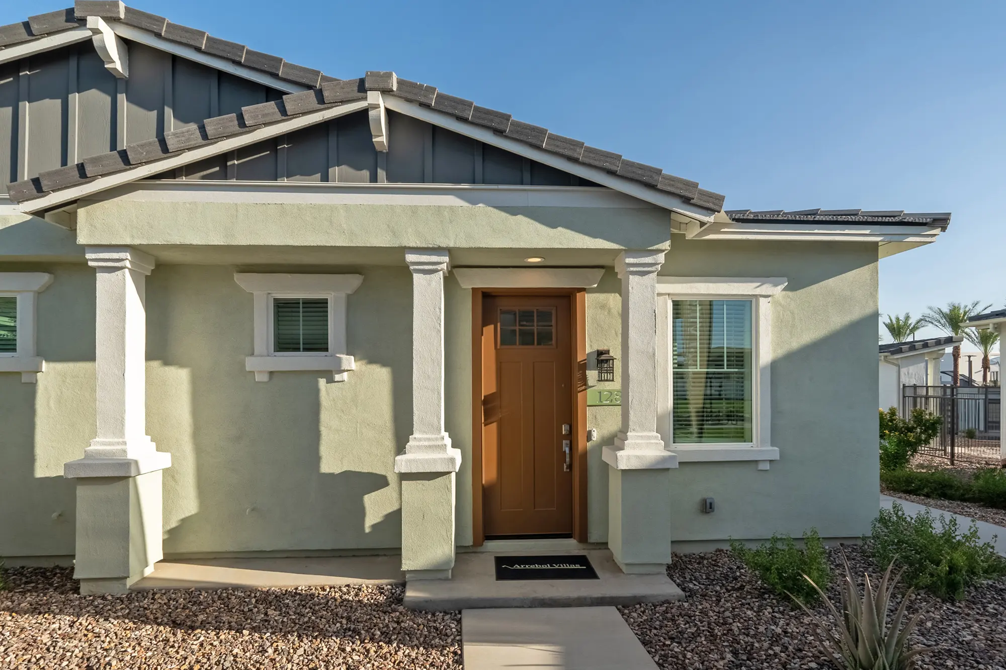 Exterior view of a modern single-story home with light green walls and a brown front door.