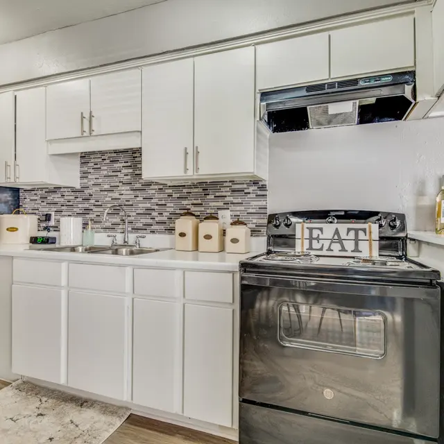 A modern kitchen with white cabinets, a black stove, and a fridge. The countertop has small decor items and a backsplash with a mosaic pattern.