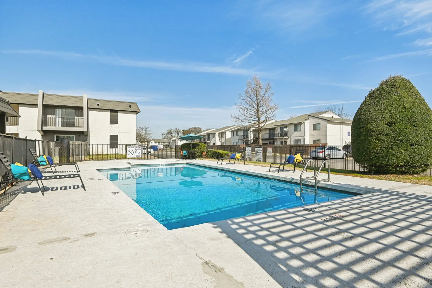A swimming pool area in an apartment complex with lounge chairs and buildings in the background.