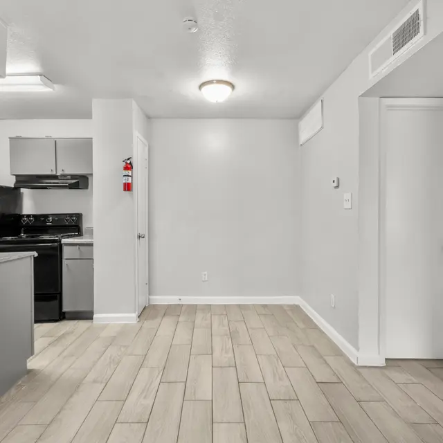 A spacious interior view of an apartment showcasing a kitchenette and living area with light wood flooring.