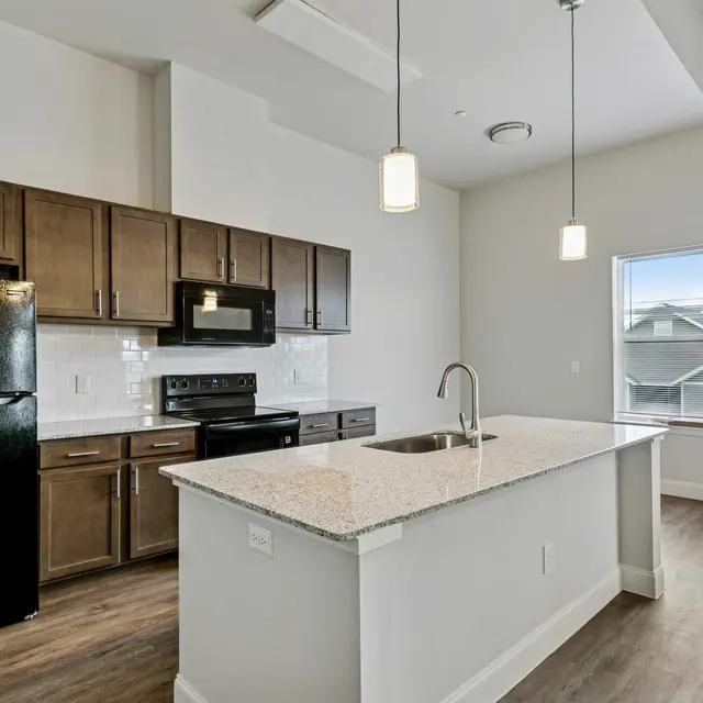 Modern kitchen with dark wood cabinets and granite countertops, featuring a black refrigerator and stove, accompanied by a large window providing natural light.