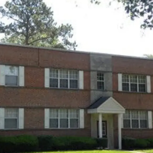 A two-story brick apartment building with white window frames and a central entrance featuring a small awning.