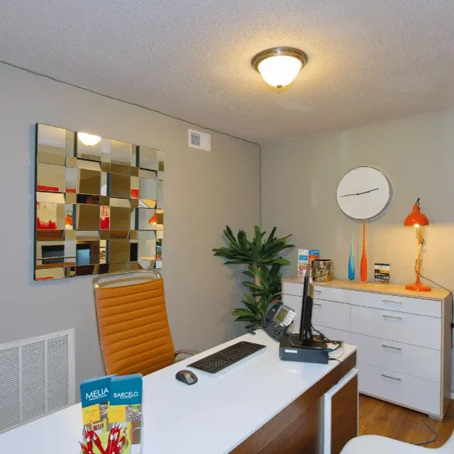 A modern office space with a stylish desk, a chair, and decorative elements. The office features a mirrored wall art, a bright orange desk lamp, and a potted plant.
