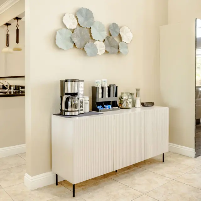 A modern kitchen corner with a white sideboard, coffee maker, and decorative wall art featuring layered circular shapes.