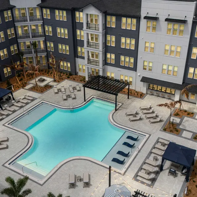 Modern Apartment Complex Pool Area Aerial view of a modern apartment complex with a central pool area surrounded by lounge chairs and shaded cabanas.