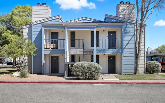 Exterior view of a two-story apartment building with a light blue facade, featuring balconies and well-maintained landscaping.