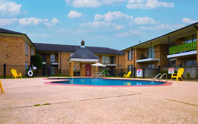 A swimming pool surrounded by a concrete deck and yellow lounge chairs in an apartment complex.