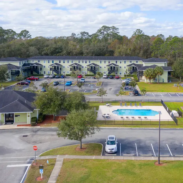 Aerial view of an apartment complex featuring two buildings, a parking lot, a swimming pool, and a playground area.