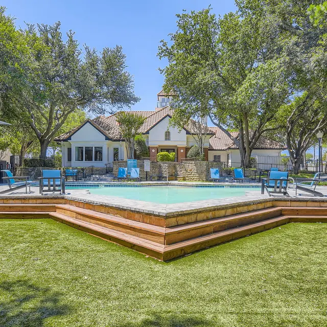 A vibrant outdoor swimming pool area surrounded by lush green grass and trees, featuring a well-maintained deck and lounge chairs.