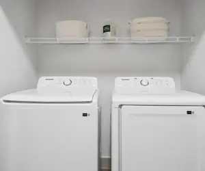Modern Laundry Room Setup A clean and organized laundry room featuring a washing machine and a dryer side by side, with a shelf above displaying storage baskets and detergent.