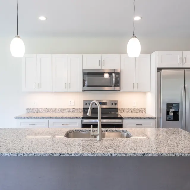 Bright and modern kitchen featuring a large island with a granite countertop, stainless steel appliances, and white cabinetry.
