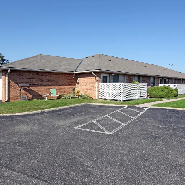 Exterior view of a single-story brick building with a parking lot and green landscaping.