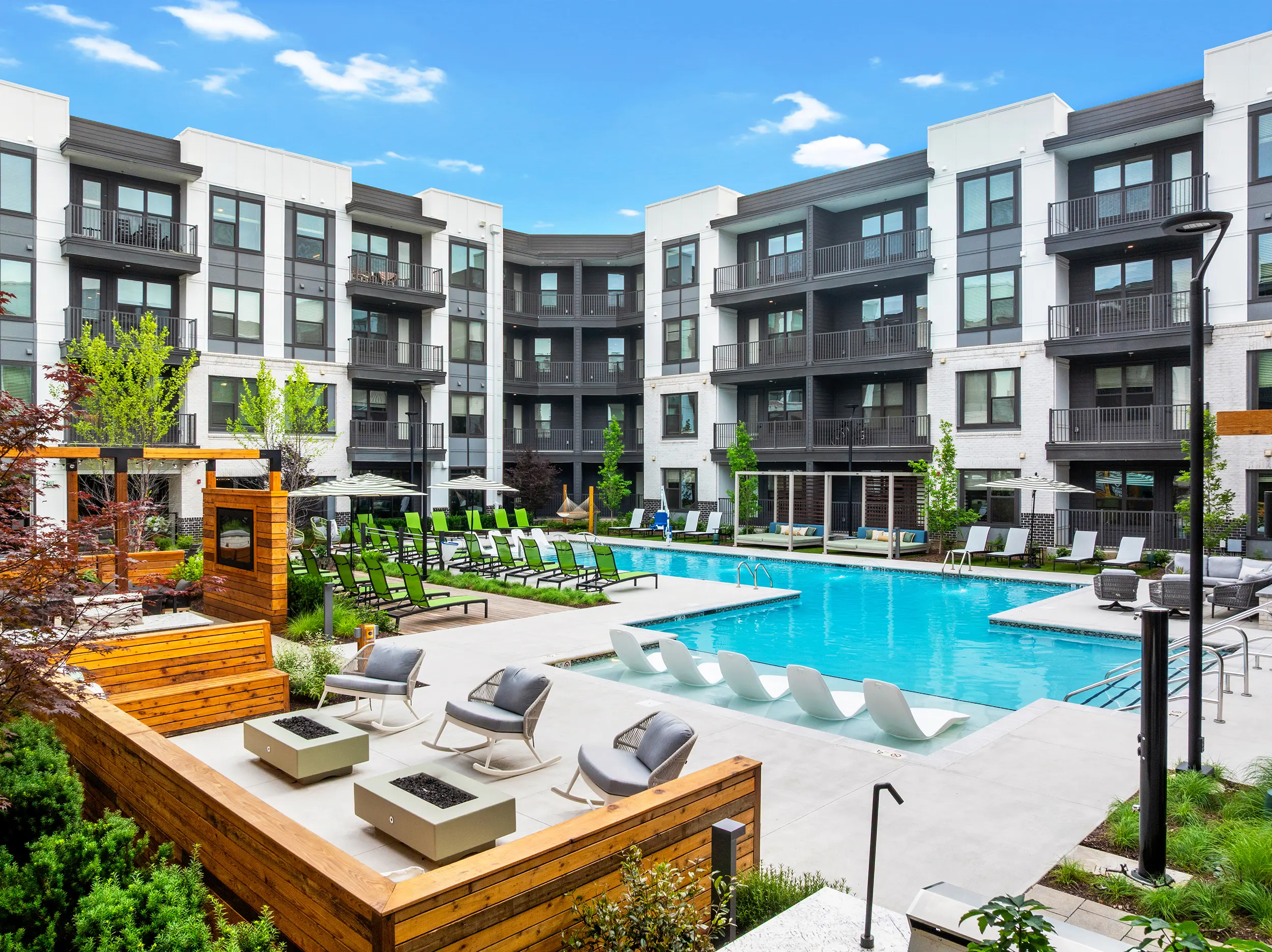 A modern apartment complex featuring a pool, lounge chairs, and landscaping.