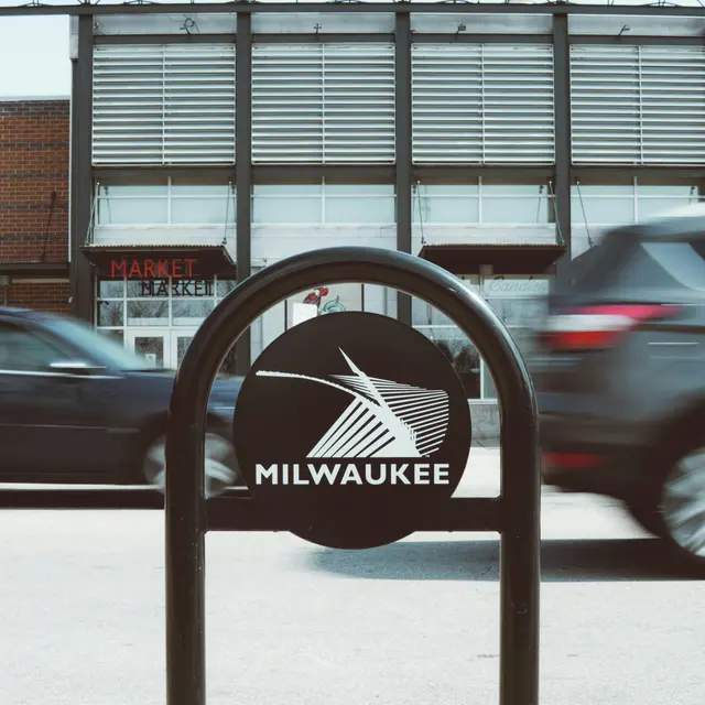 Milwaukee Public Market View of a street sign for Milwaukee with the Milwaukee Public Market in the background, featuring large letters that read 'MILWAUKEE PUBLIC MARKET'. Cars are passing by in front of the sign.