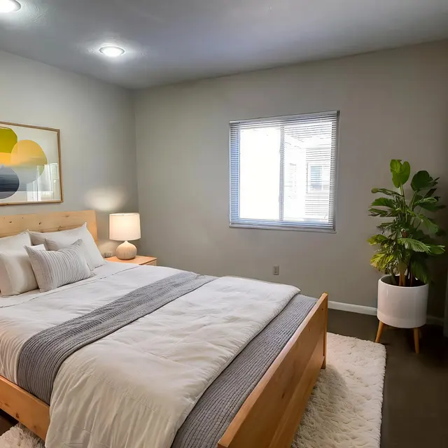 A modern bedroom featuring a wooden bed with white bedding, nightstands with lamps, a large window, and a potted plant.