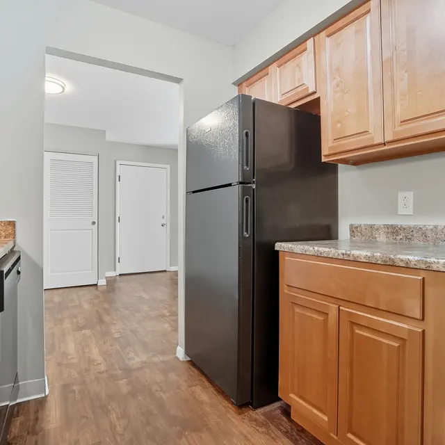 A modern kitchen featuring dark appliances, wooden cabinetry, and a view into a hallway with doors.