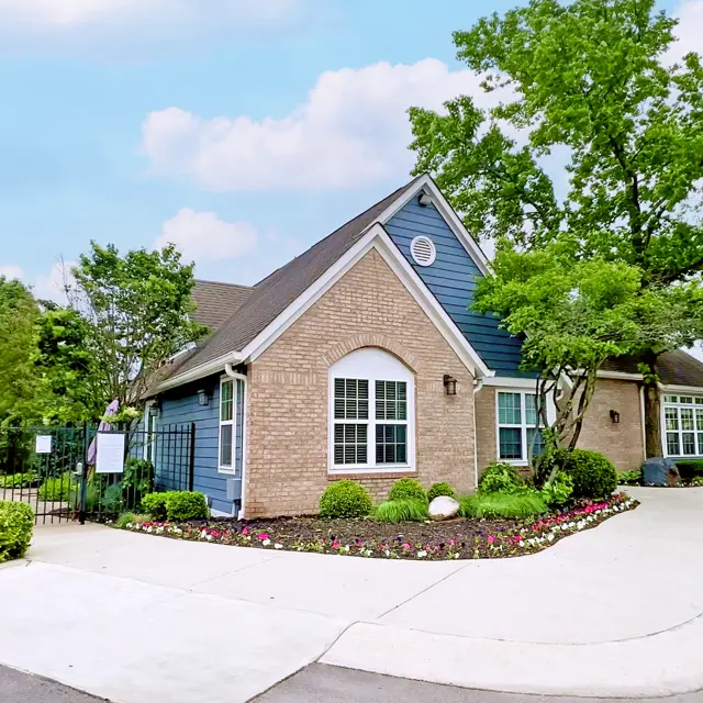 A well-maintained residential building with a blue exterior and landscaped gardens, featuring trees and colorful flowers in front.