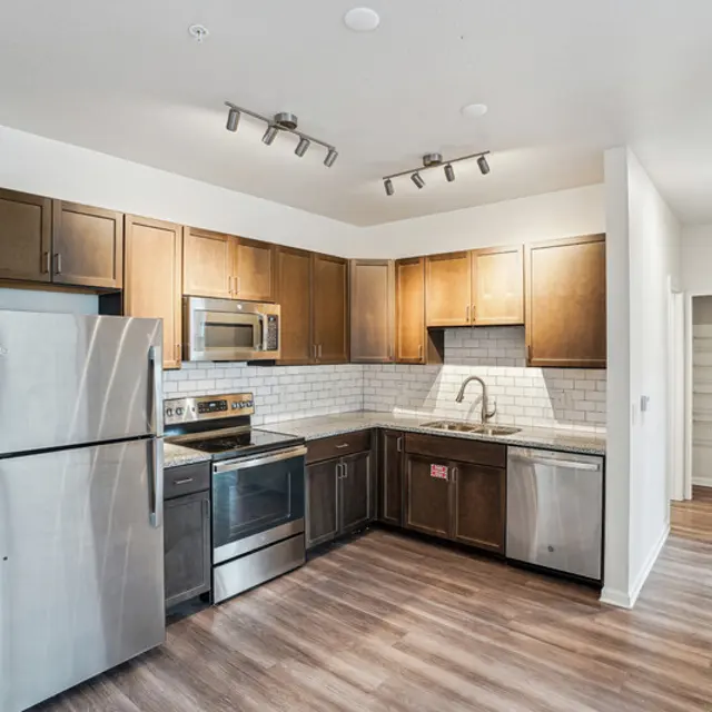 Modern kitchen with dark wood cabinetry, stainless steel appliances, and hardwood floors, featuring a sink and a spacious layout.