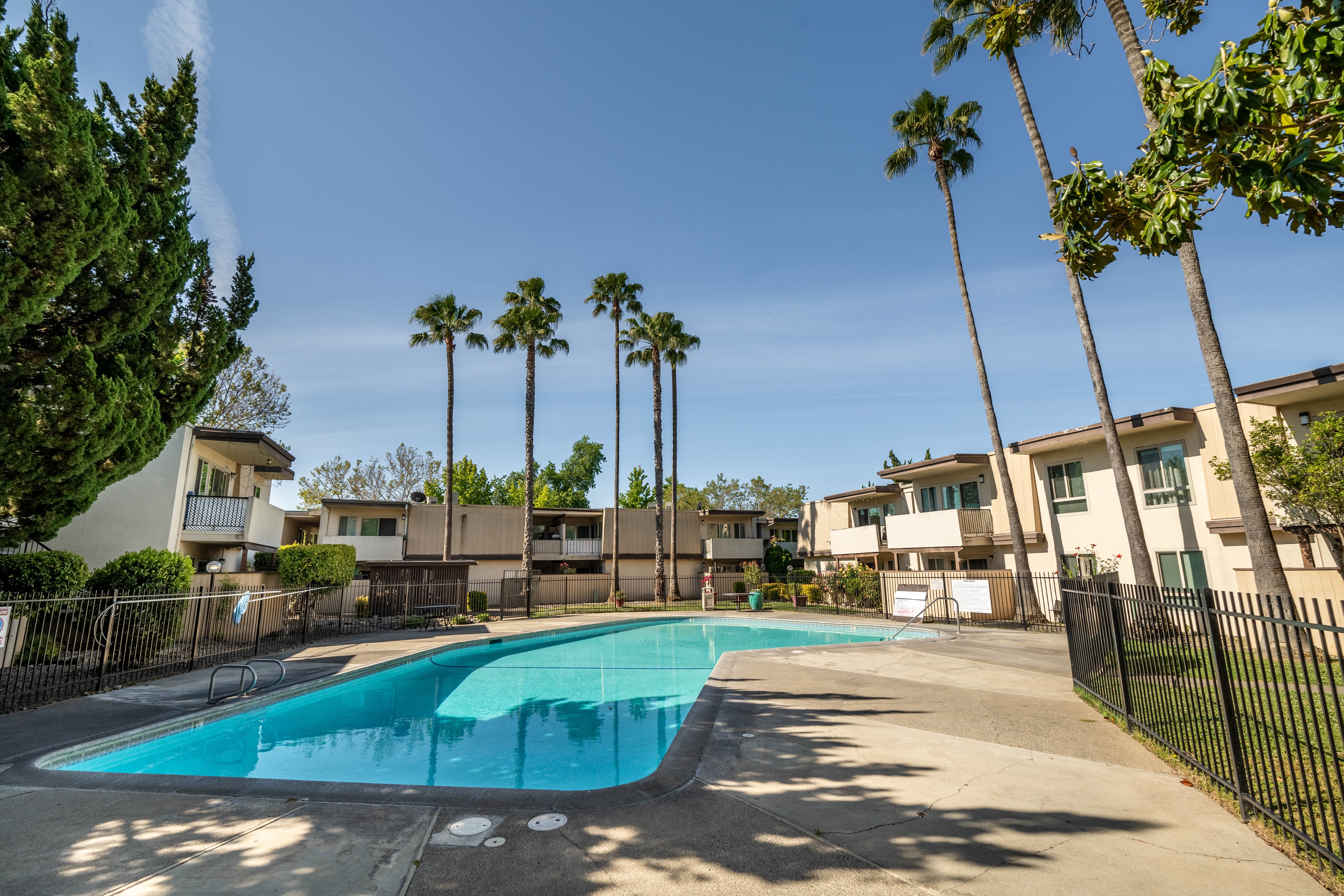 A residential apartment complex featuring a swimming pool surrounded by palm trees and buildings.