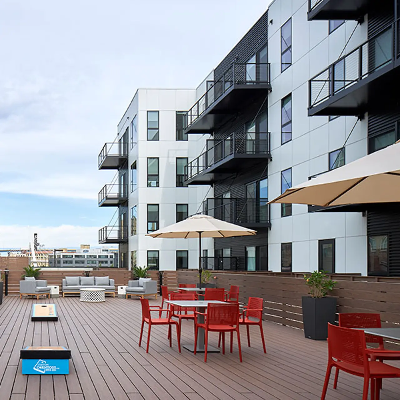 Modern Rooftop Terrace A modern rooftop terrace featuring wooden flooring, red chairs, tables, and large umbrellas, with contemporary buildings in the background.