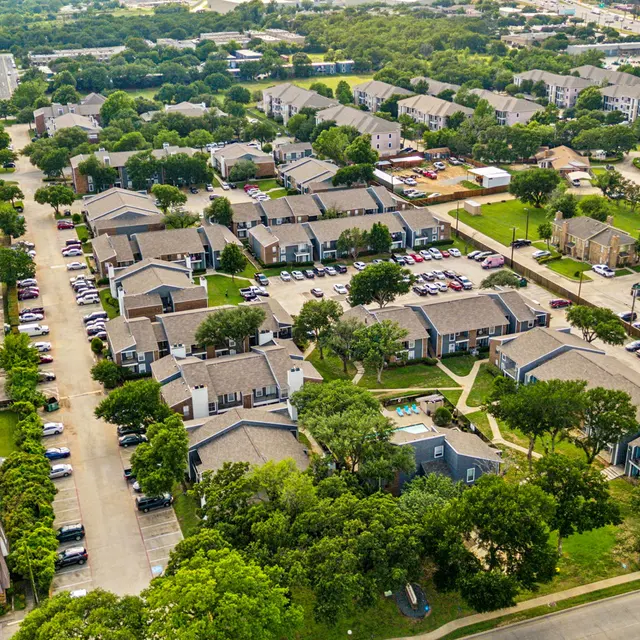 Aerial view of a residential community with multiple buildings, green trees, and a nearby road.