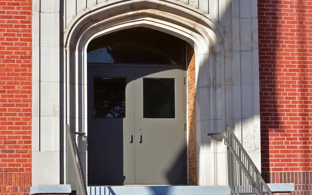 Harrison School Entrance Entrance of Harrison School featuring a brick building with a prominent archway, steps, and two doors.
